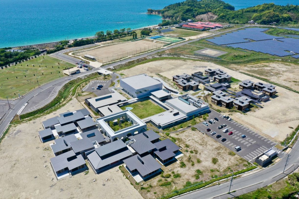 平屋の建築群が瀬戸内海を臨む広島叡智学園の全景。中庭を囲んで職員棟、体育館、カフェテリアなどが配された中央エリア、図書館を軸とした教室エリア（左側）、メゾネットタイプの寮ハウスが連なる居住エリア（右側）に分かれる（同学園提供）