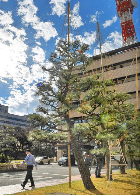 降雪に備え雪つりの設置作業が行われる中、強い日差しの下を軽装で歩く人=県庁で
