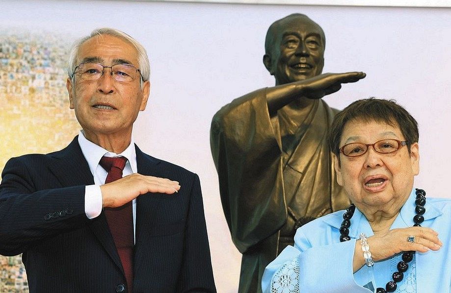 志村けんさんの銅像の前でアイーンのポーズを決める兄の知之さん（左）と高木ブー