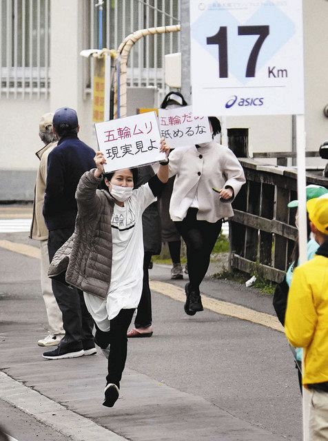 東京五輪マラソンテスト大会のコース沿道で、「五輪ムリ」などと書かれたメッセージを掲げる人たち（代表撮影）