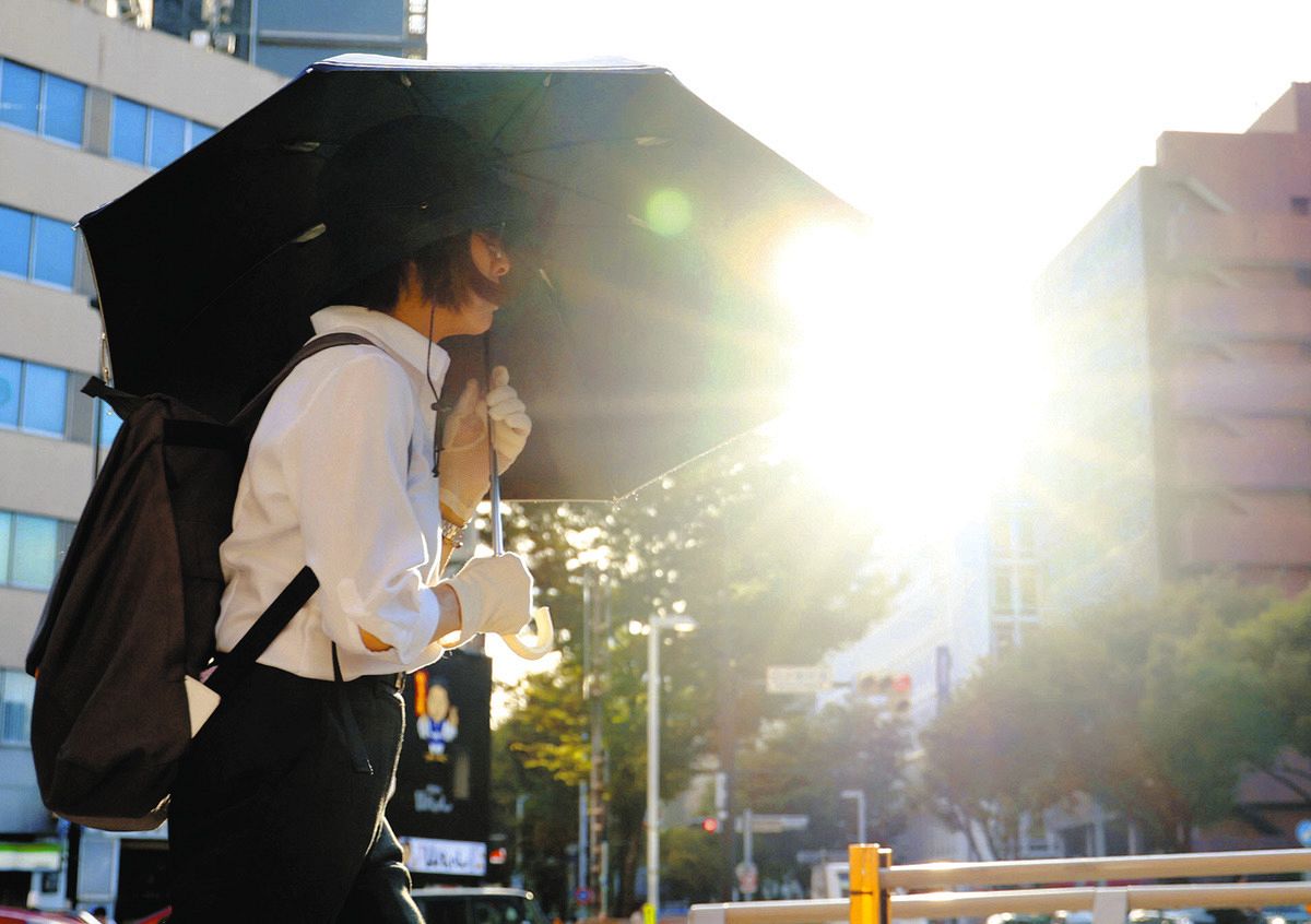 体温を超えるような暑さになり、西日に日傘を差して歩く人＝18日、名古屋市中区で（伊藤遼撮影）