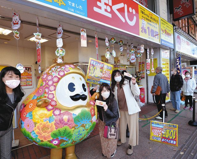 買ったばかりの宝くじを手にひゃくまんさんと記念写真に納まる女性たち＝２４日午前、金沢市武蔵町で 