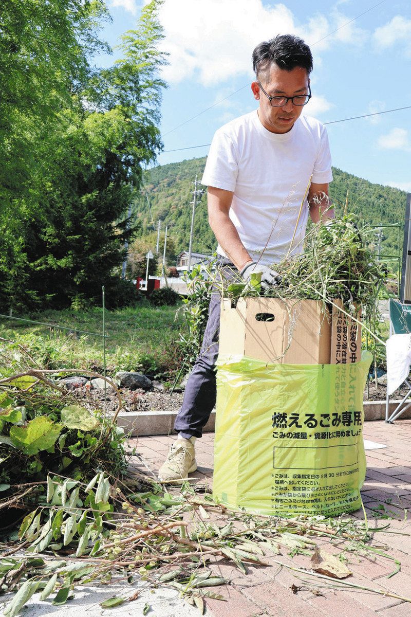 商品を使ってごみ袋に草や枝を入れる越農さん＝中津川市付知町で
