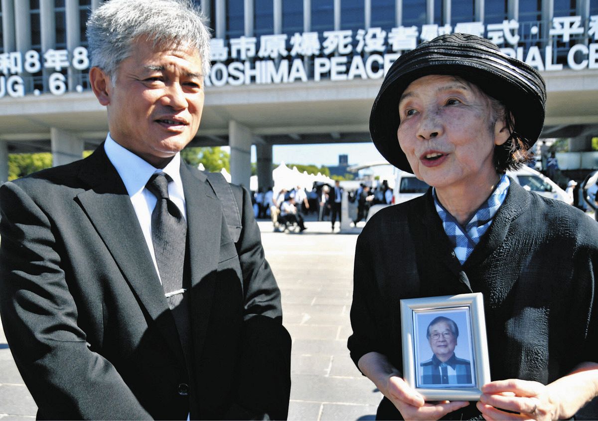 平和記念式典の会場で、夫靖弘さんの遺影を手に平和を願う三浦節子さん（右）と靖樹さん＝6日、広島市中区で