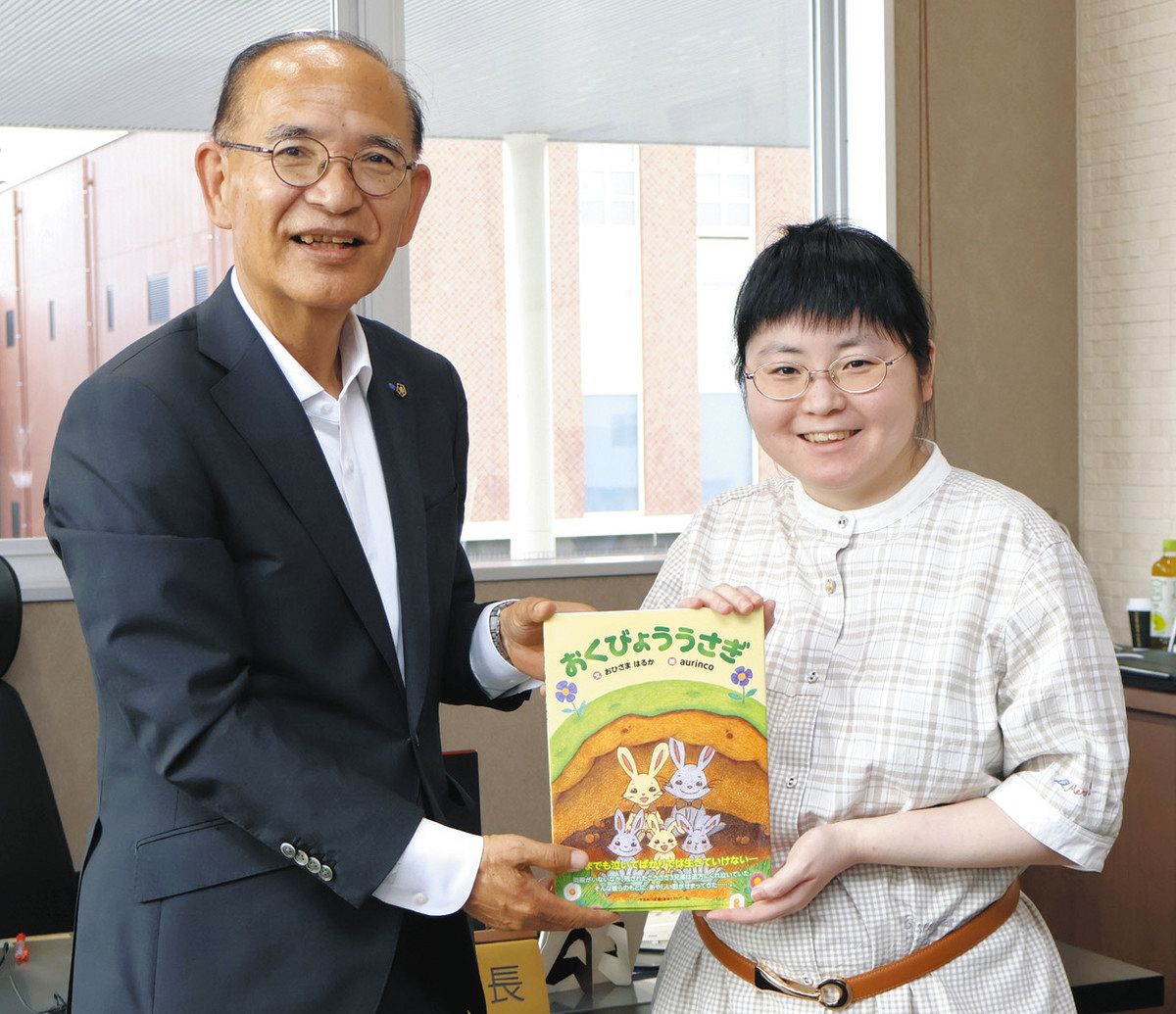 仙石教育長（左）に絵本を手渡した高橋さん＝多治見市役所駅北庁舎で