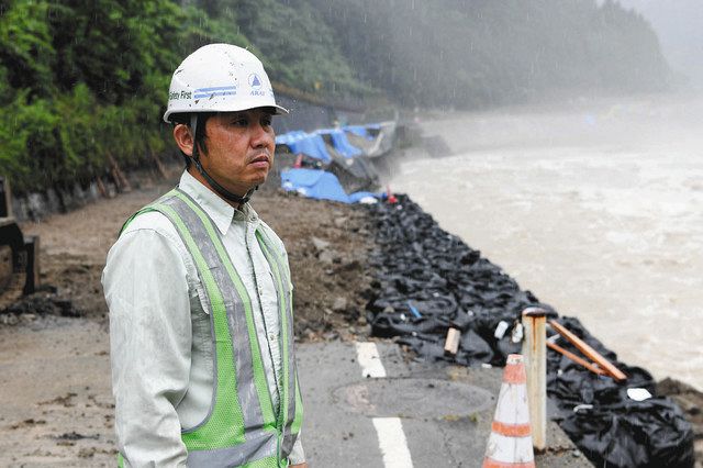 崩落した国道４１号を背に、増水した飛騨川を見つめる今村さん＝下呂市小坂町門坂で 