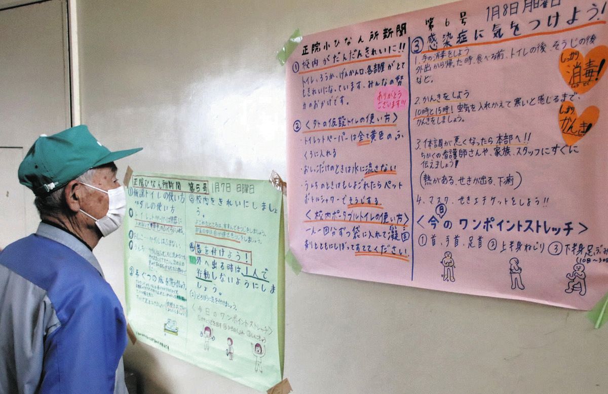 壁新聞を読む避難者＝9日、石川県珠洲市正院小で