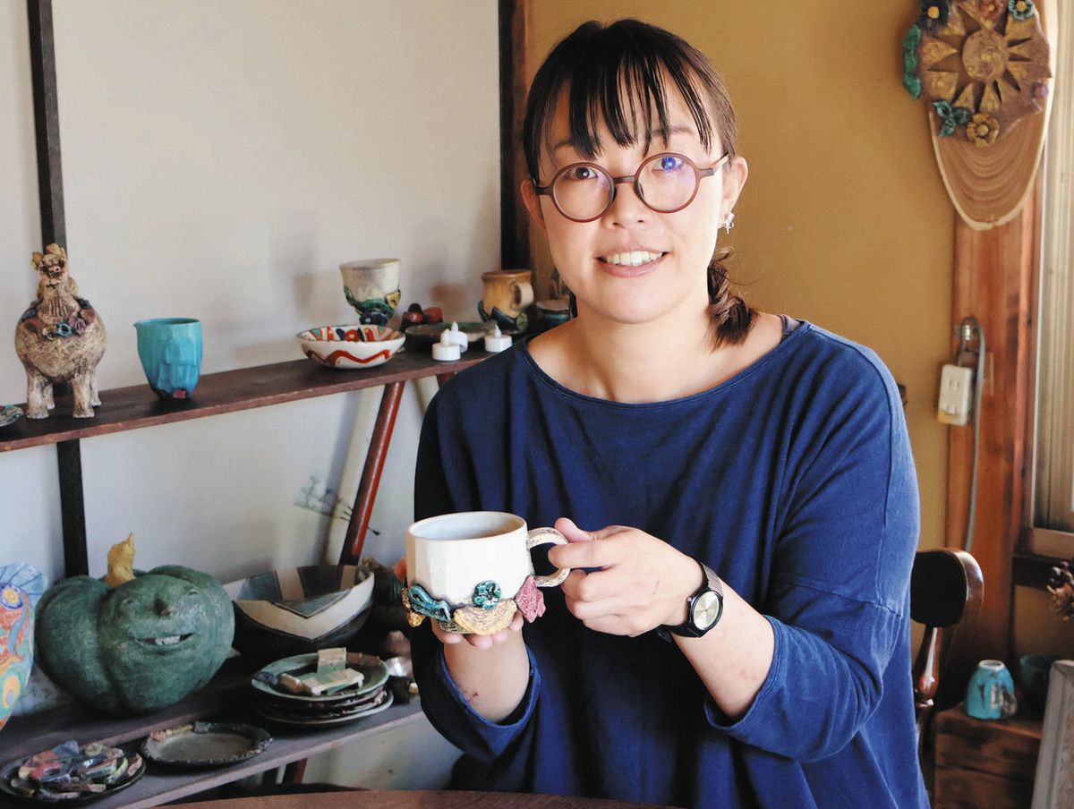 自身の作品をバックに、出品するコップを手にする牧野さん＝瑞浪市釜戸町で