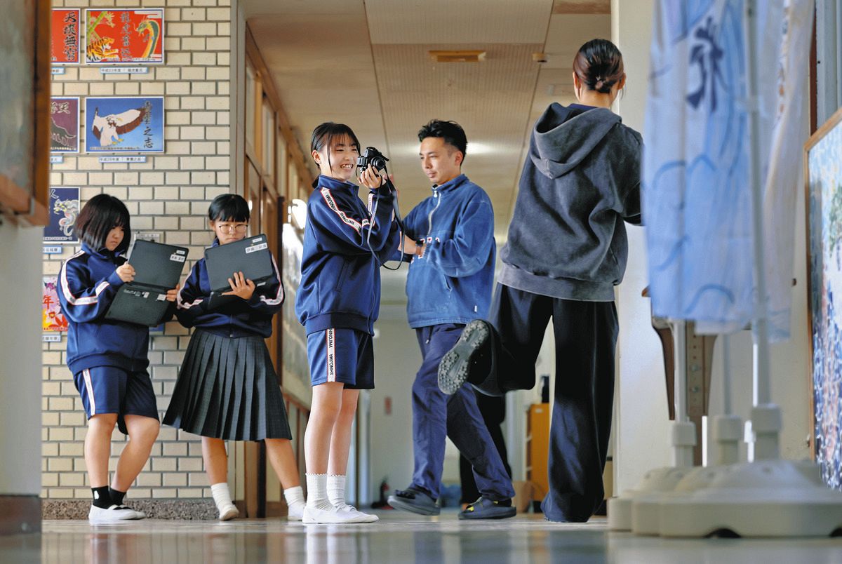 玄関近くに掲示する教員紹介のため、写真を撮影するボランティア部の新美さん（中）