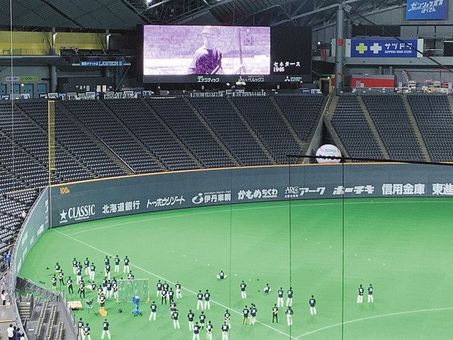 球場の大型ビジョンに写る球団の歴史を伝える映像を見入る日本ハムの選手ら