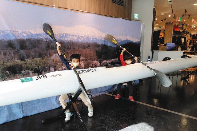 東京五輪男子カヤックフォアで日本代表選手が使ったパドルを持ち、カヌー艇と記念撮影をする子どもたち＝小松市清六町で 