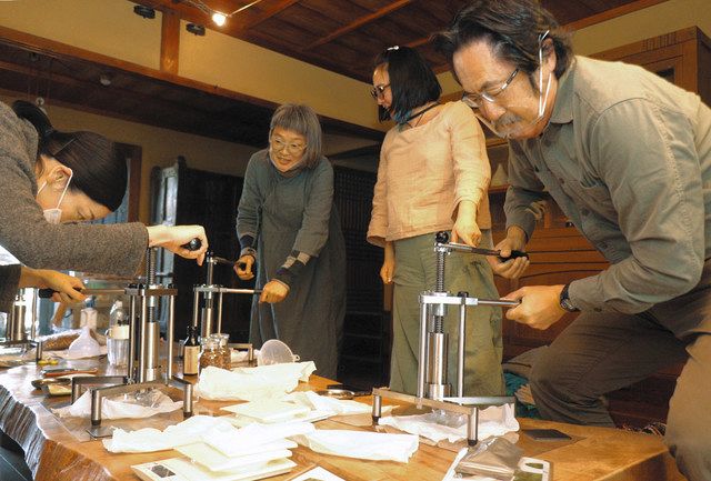 圧搾機で茶の実から油を搾る山田さん（右）と参加者たち＝亀山市関町中町の而今禾で 