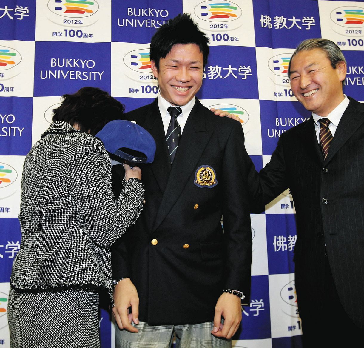 記念撮影で、間違えて帽子をかぶってしまった母早苗さんに抱きつかれ苦笑いの大野雄大（中）。右は中田スカウト部長
