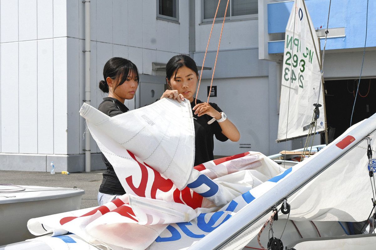 メインセール（主帆）を上げる笑莉さん（右）と奈羅さん＝津市柳山津興の津ヨットハーバーで