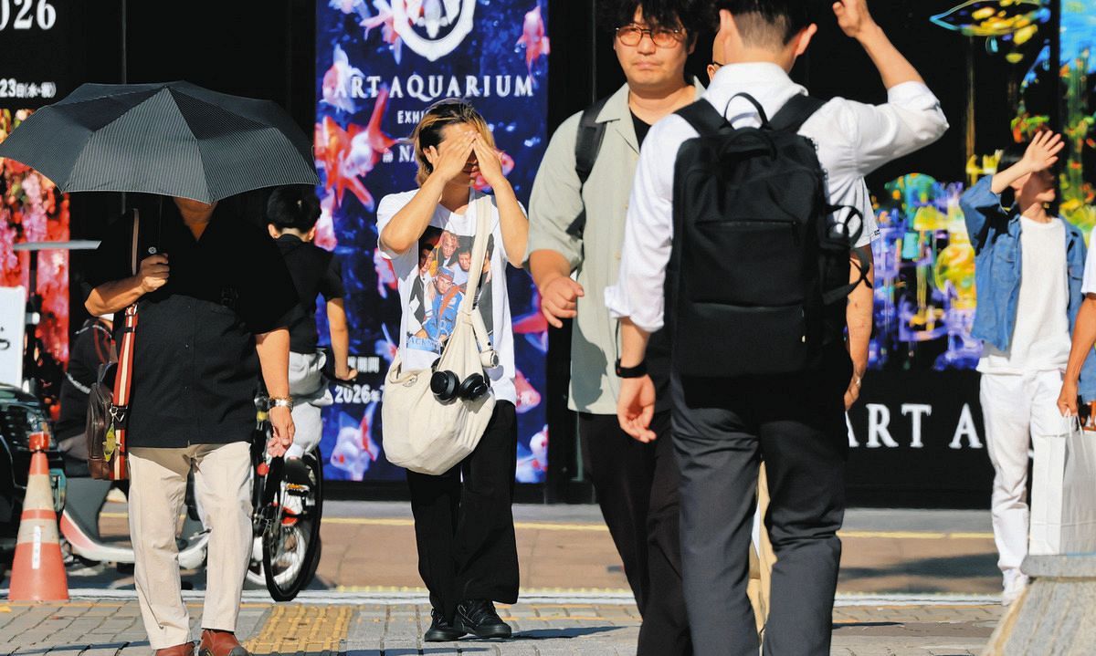 厳しい暑さの中、手で日差しを遮ったり日傘を差して歩く人ら＝名古屋・栄で