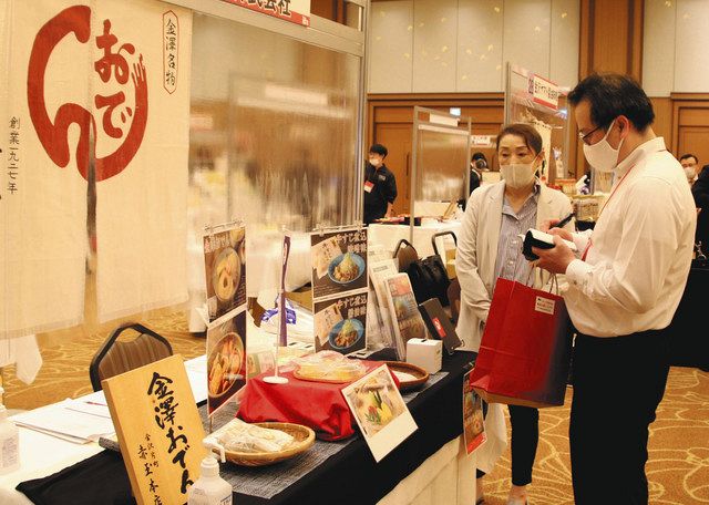県産の加工品や農産物が並ぶ商談会の会場でメモを取る参加者（右）＝金沢市内で 