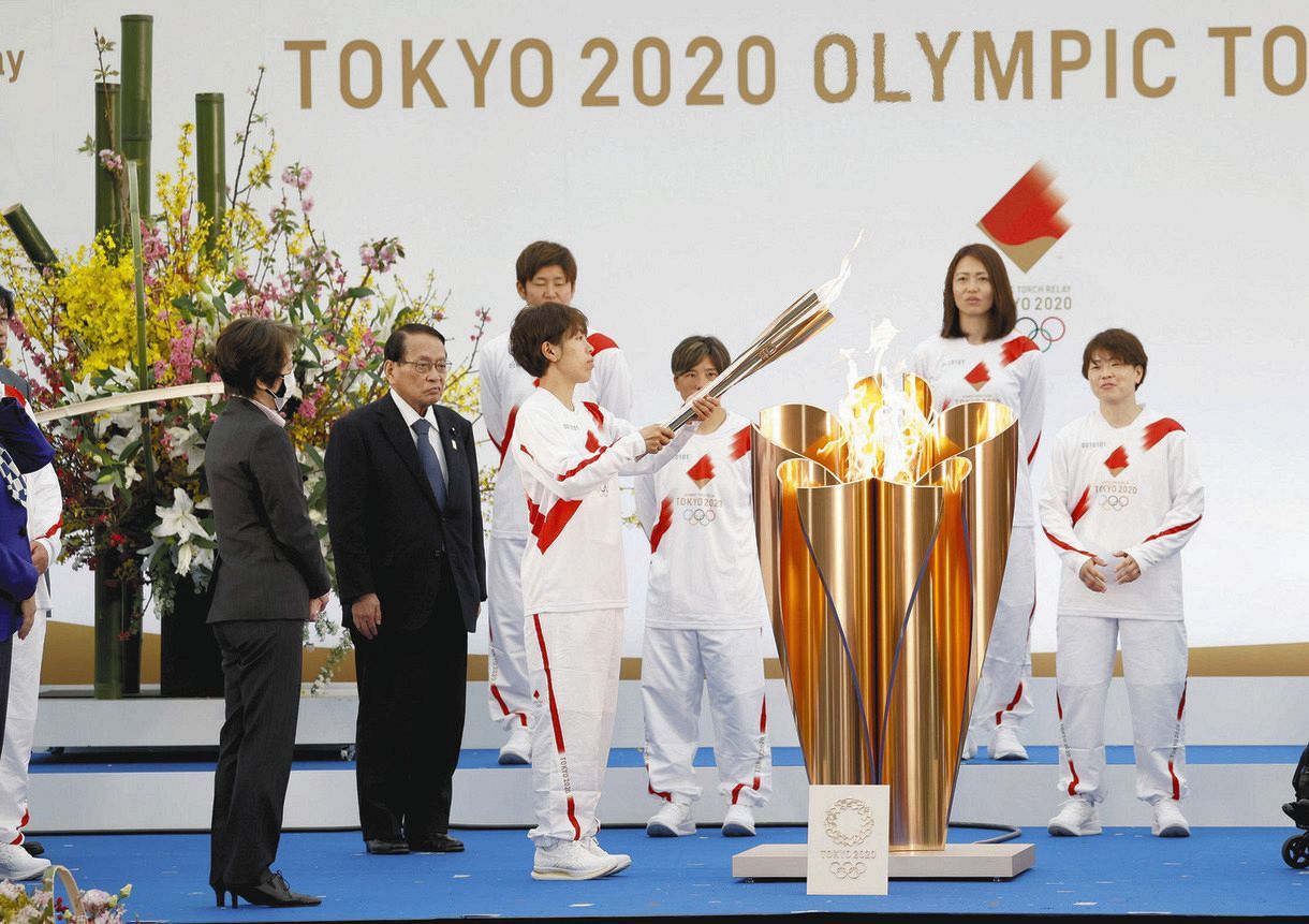 聖火リレーの出発式でトーチに火をともす「なでしこジャパン」メンバーの岩清水梓選手（中央左）＝代表撮影