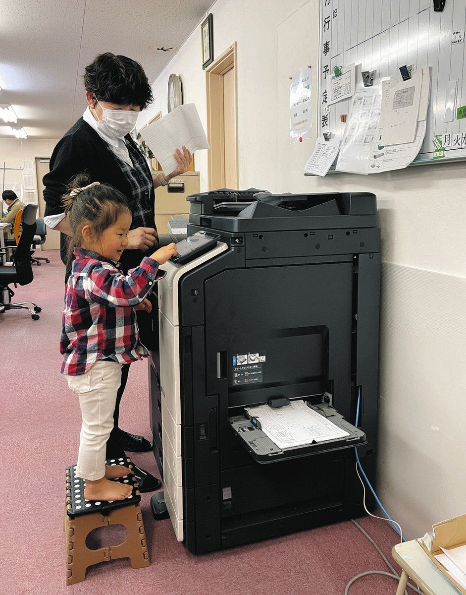 コピー機を操作して仕事の手伝いをする「子連れ出勤」の子ども（手前）＝土岐市泉町久尻の向陽信和で（向陽信和提供）
