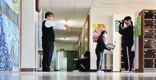 「両手を前に」と指示を受け、ボランティア部員の写真撮影に臨む岩崎教頭（左）