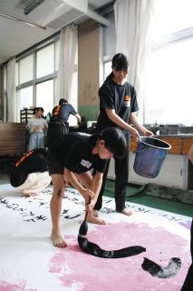 大きな筆で文字を書く小学生（手前）＝飯田市上郷黒田の飯田高で
